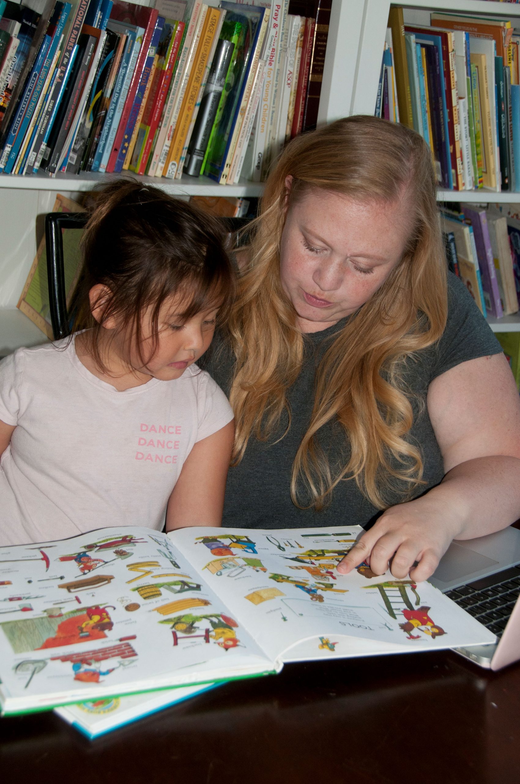 Ally Adair-Chung reading a homeschool book with her daughter at a table.